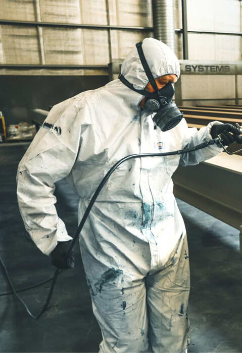 Travailleur en combinaison de protection appliquant peinture industrielle sur de l'acier dans une usine